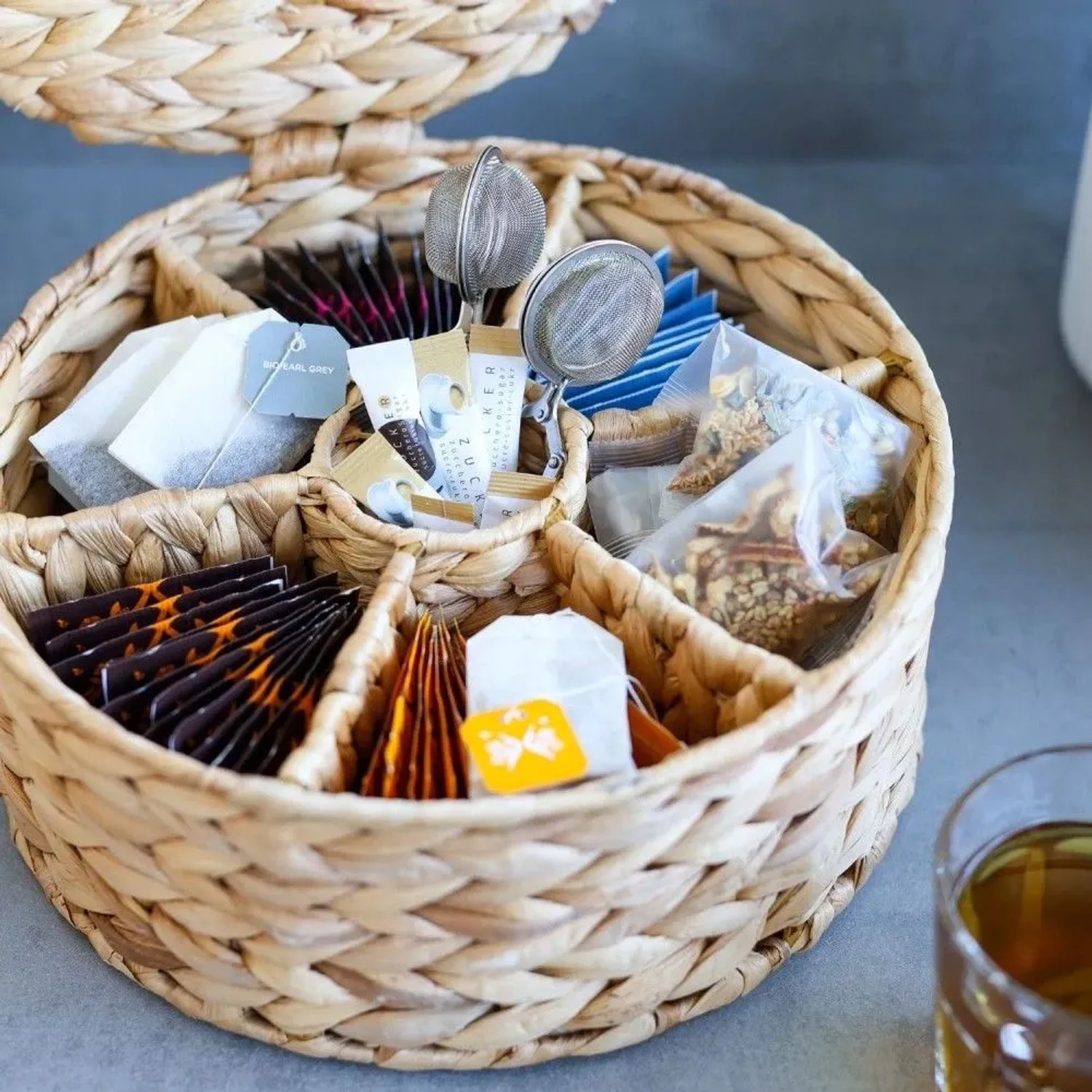 Runde Teebox aus geflochtener Wasserhyazinthe mit 7 Fächern, gefüllt mit Teebeuteln und Zuckersticks. Praktische Aufbewahrungsbox.