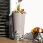 Arves Regentonne Rainbowl Flower 150 l Taupe mit Bepflanzung und Gießkanne vor weißer Wand.