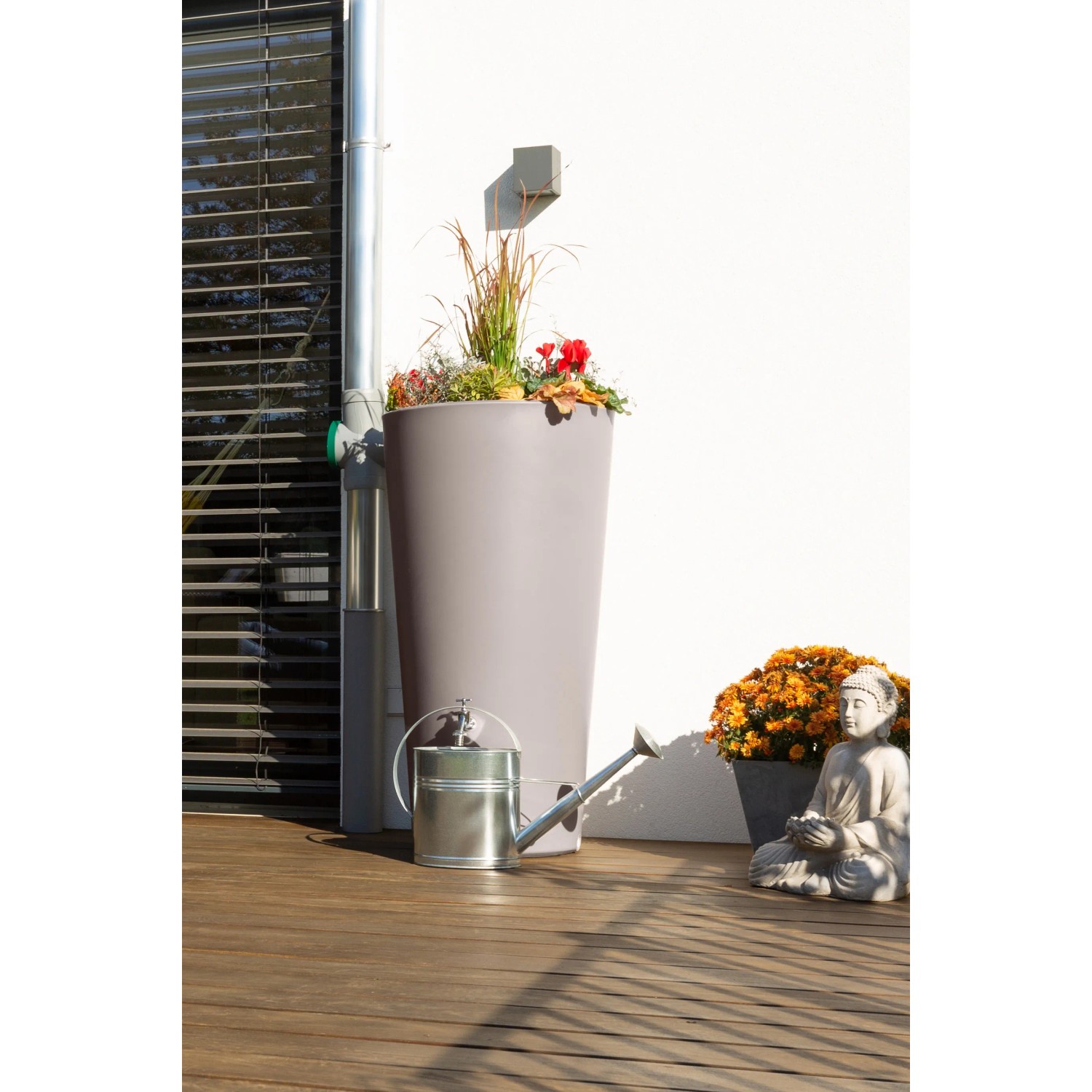 Arves Regentonne Rainbowl Flower 150 l Taupe mit Bepflanzung und Gießkanne vor weißer Wand.