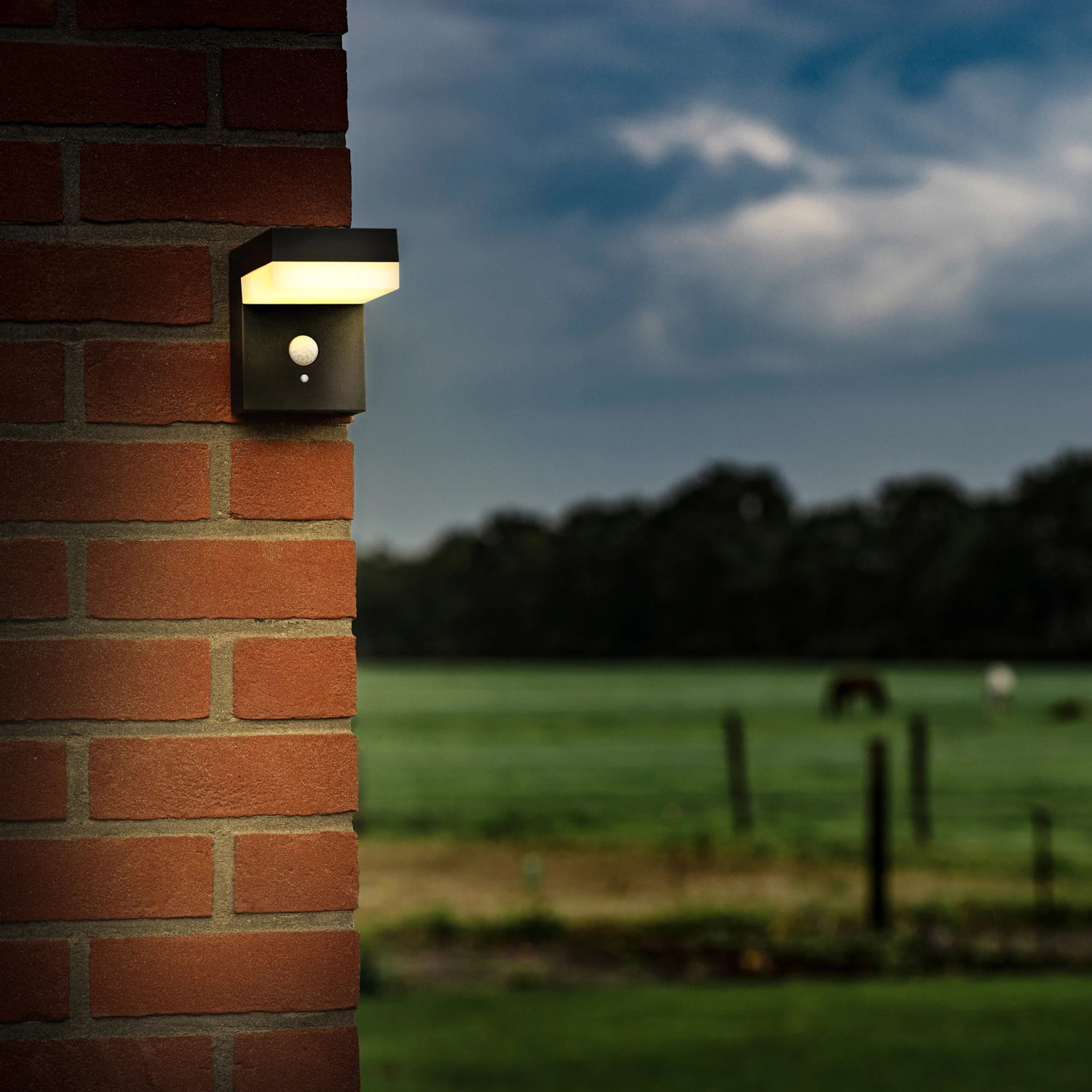 Schwarze Solar-Wandleuchte mit Sensor an einer Backsteinwand im Außenbereich.