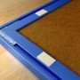 Detailansicht: Blauer Bilderrahmen mit Fischer Montagestreifen zur Befestigung.