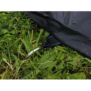 Schwarze Abdeckplane für rechteckiges EXIT Trampolin, befestigt mit Hering im Gras.