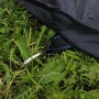 Schwarze Abdeckplane für rechteckiges EXIT Trampolin, befestigt mit Hering im Gras.