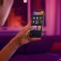 Frau steuert Philips Hue Lampe E14 per App auf Smartphone. Smart Home Beleuchtung.