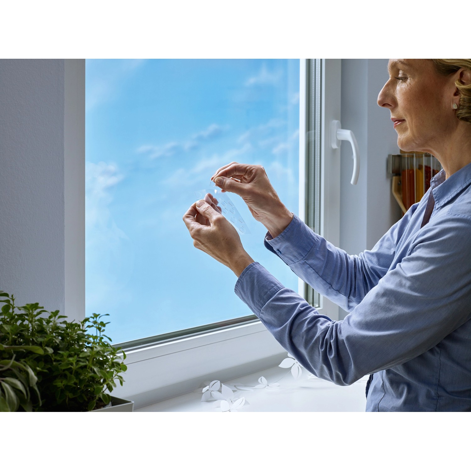 Frau befestigt Tesa Klebepad auf Glas. Doppelseitige, transparente Klebepads für Fenster.