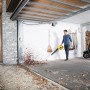 Mann benutzt gelben Kärcher Akku-Laubbläser LBL 4 Battery zum Laub entfernen vor Garage.