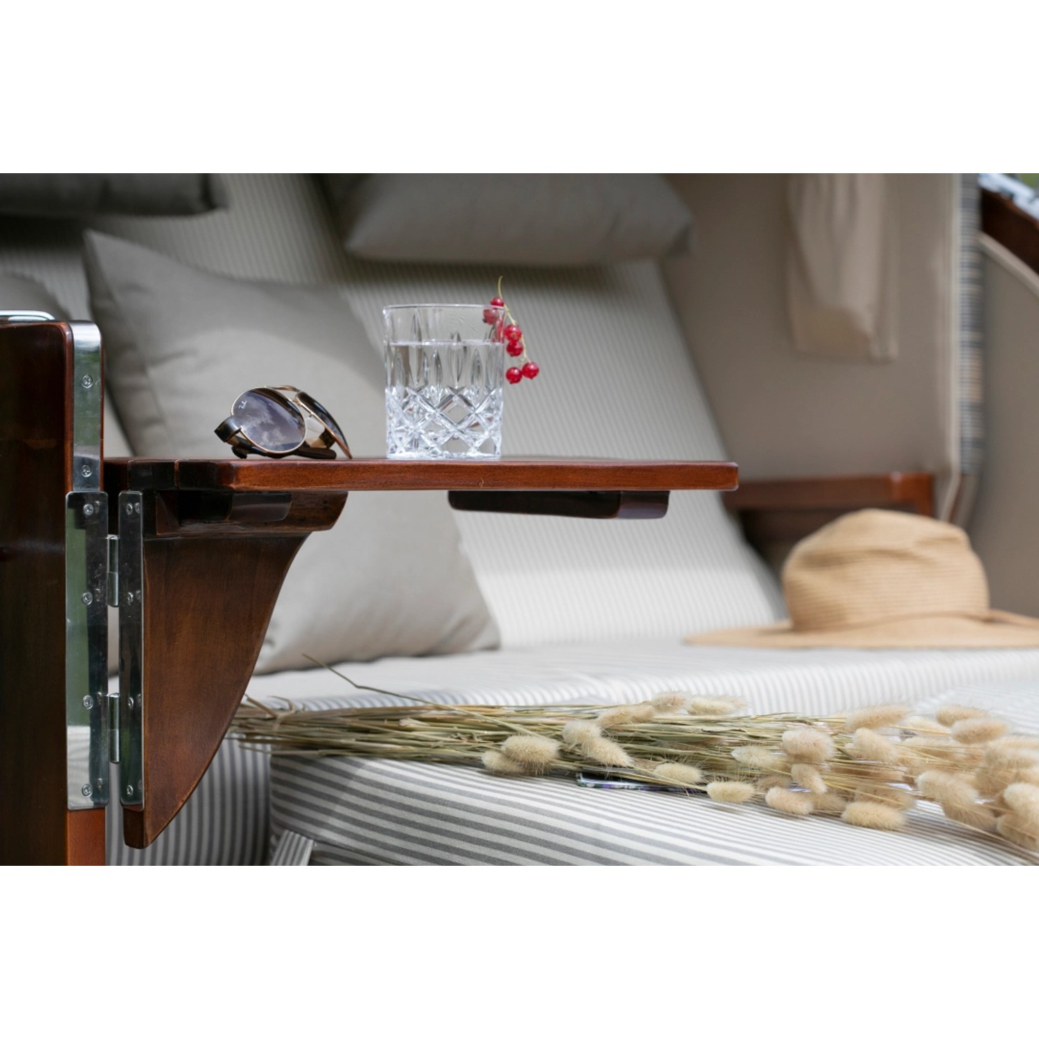 Detailaufnahme: Mahagoni Strandkorb Westerland mit Bullauge, Tisch mit Getränk und Deko.