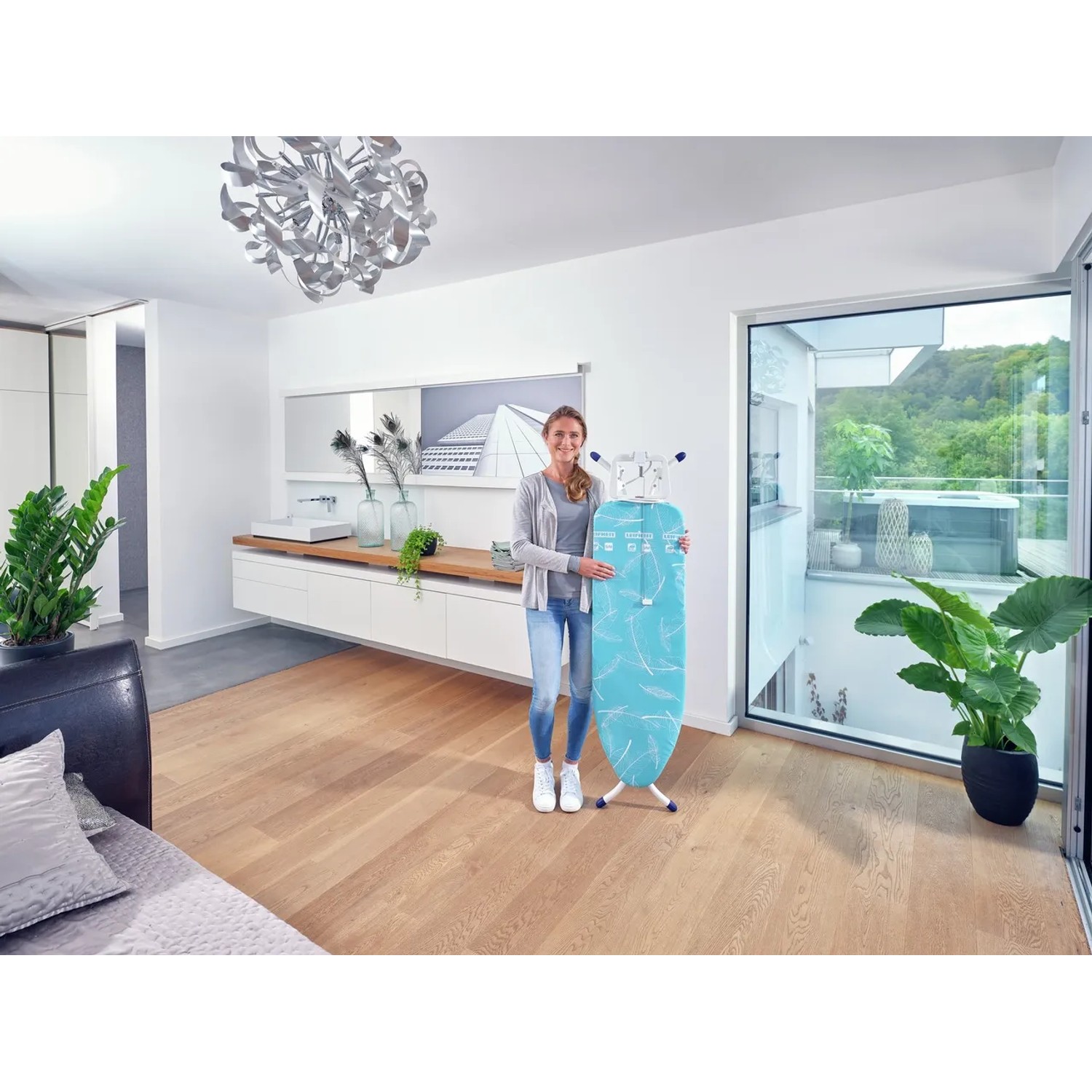 Frau hält Leifheit Bügeltisch AirBoard Compact M Plus mit blauem Bezug. Kompaktes, höhenverstellbares Bügelbrett.