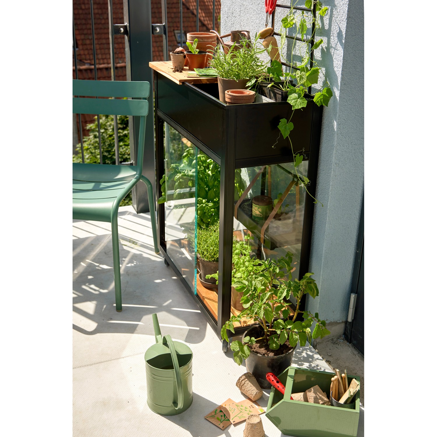 Juliana Gewächshaus Urban Vertical auf Balkon mit Pflanzen, Gießkanne und Stuhl.