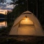 Beiges Campingzelt mit Moskitonetz, innen beleuchtet, am Seeufer bei Dämmerung. Schnellaufbau Zelt für 3-4 Personen.