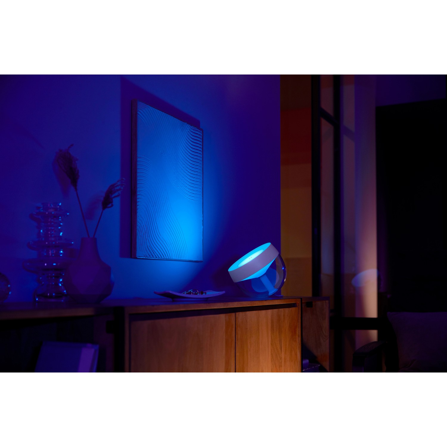 Philips Hue Iris Tischleuchte in Weiß mit blauem Lichtschein auf einem Sideboard.