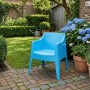 Blauer DELUKE Gartenstuhl HENRI aus Kunststoff auf gepflasterter Terrasse im Garten. Stapelbarer Outdoor-Stuhl.