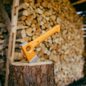 Fiskars X-series Universal-Axt X13, 35,5 cm, auf Holzscheit vor Holzstapel. Kompakte Axt für Camping und Outdoor.