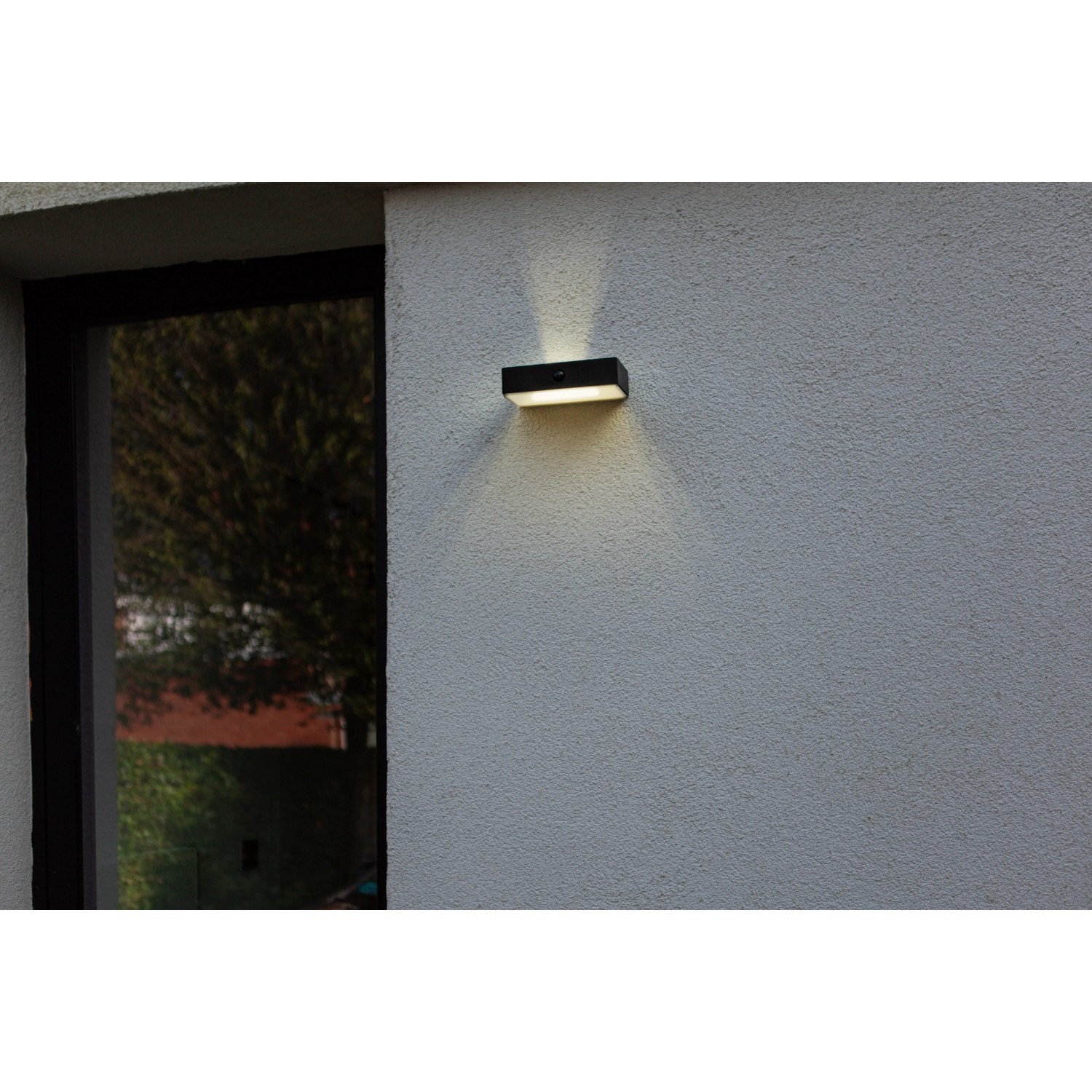 Schwarze Lutec LED Solar Wandleuchte Fadi mit Bewegungsmelder an grauer Hauswand.