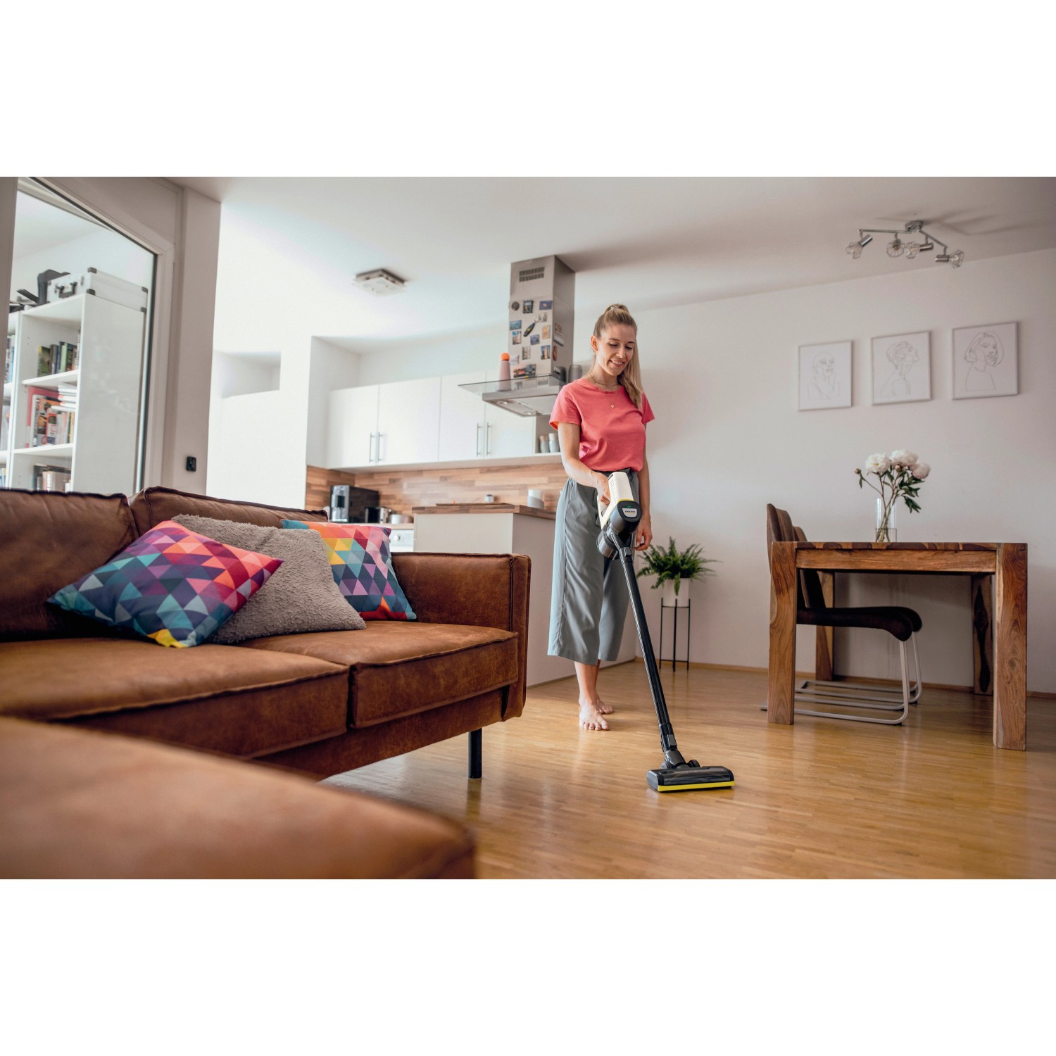 Frau saugt mit Kärcher Akku-Staubsauger VC 4 Cordless myHome Holzboden im Wohnzimmer.