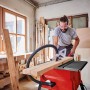 Einhell Tischkreissäge TC-TS 2025/3 Eco im Einsatz mit Holzwerkstück. Rote Tischkreissäge mit Mann im Hintergrund.