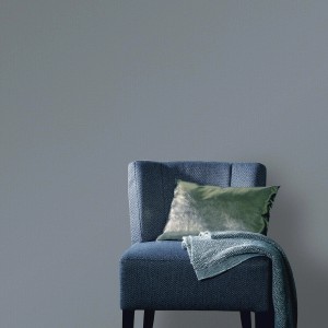 Dunkelgraue Vliestapete in Leinenoptik an Wand, kombiniert mit blauem Sessel und Kissen.