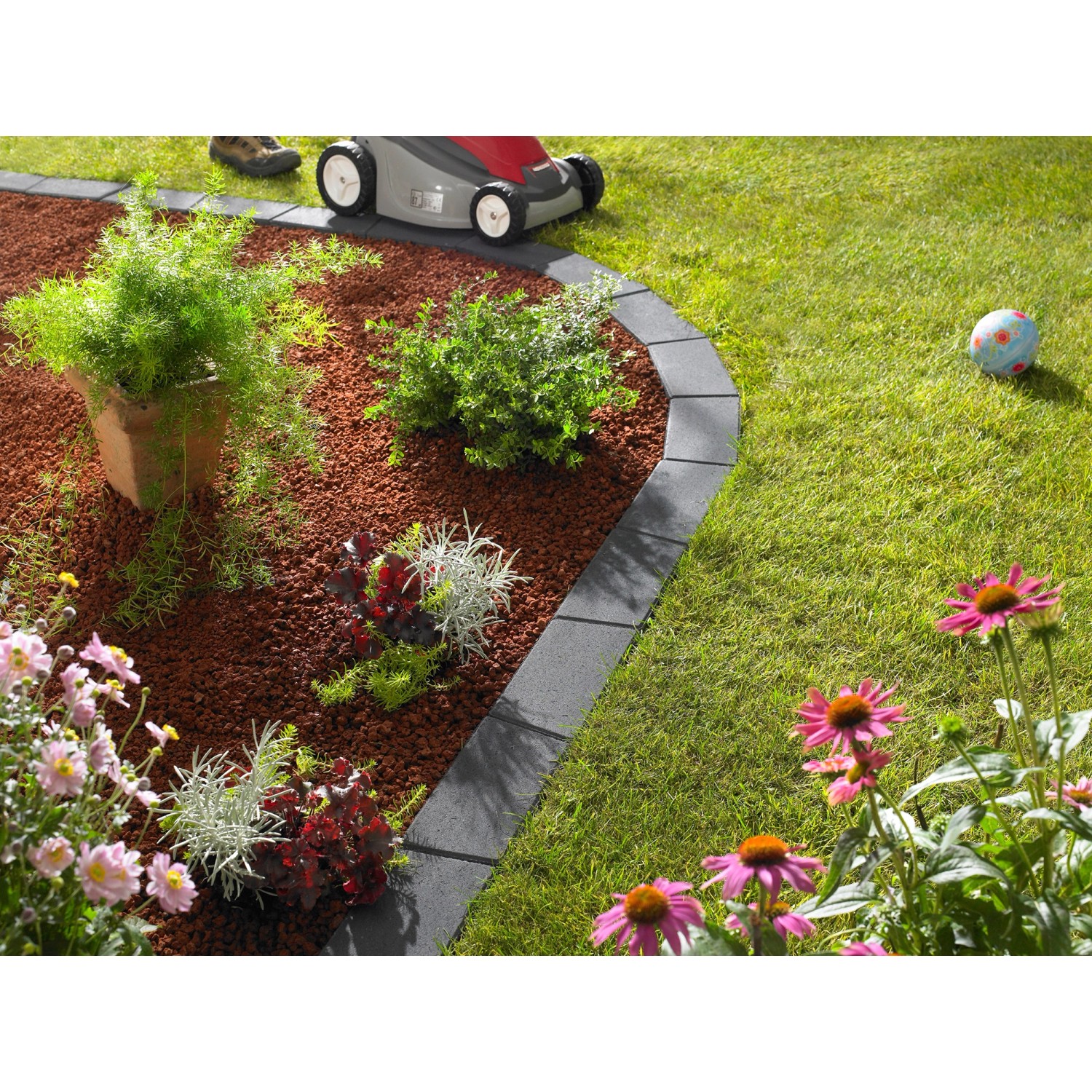 Anthrazitfarbene Kann Mähkante Vigneto als Rasenkante im Garten mit Blumen und Rasenmäher.