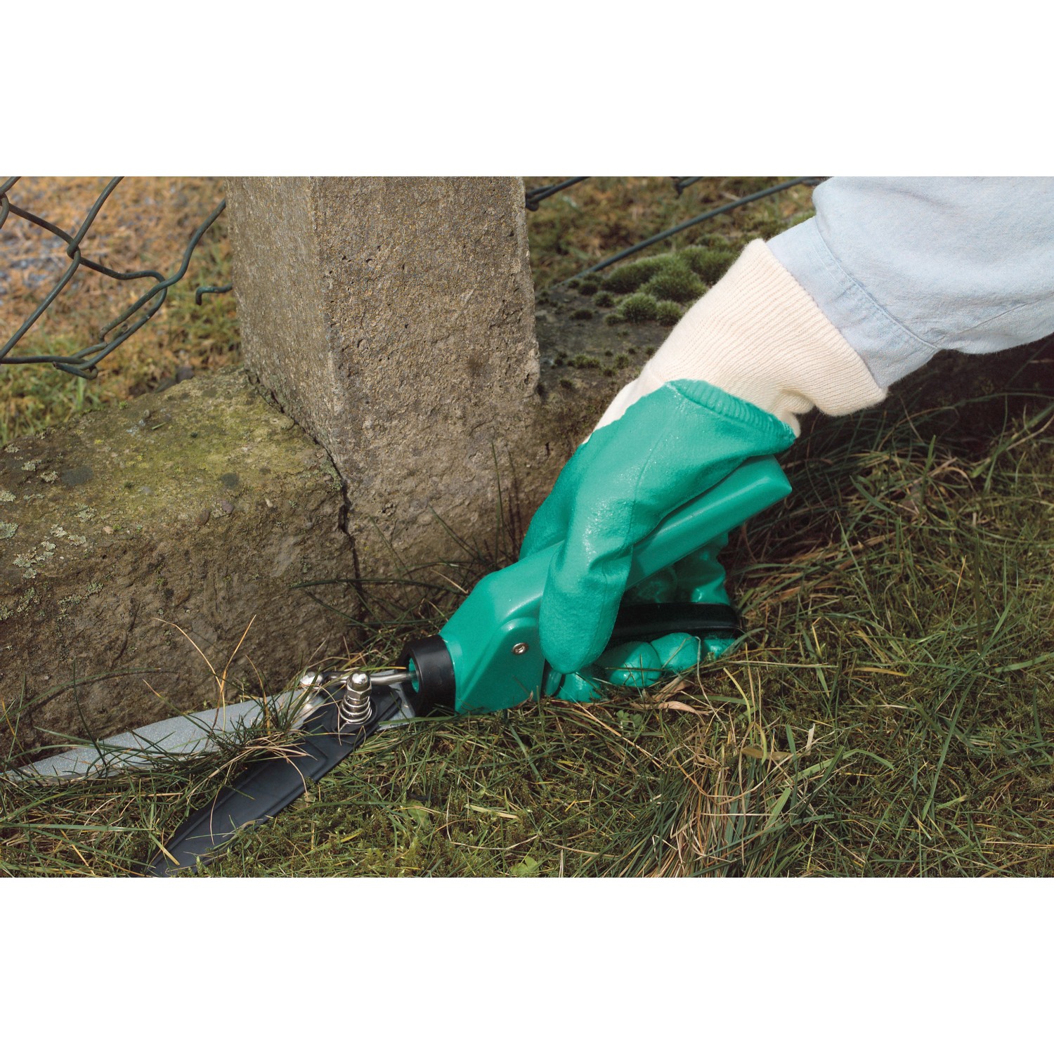 Hand mit LUX Garten Nitrilhandschuh S beim Grasschneiden. Gartenbekleidung für sicheres Arbeiten.