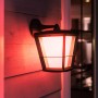 Hängende Philips Hue Econic LED-Laterne in Schwarz mit farbigem Licht an Hauswand.