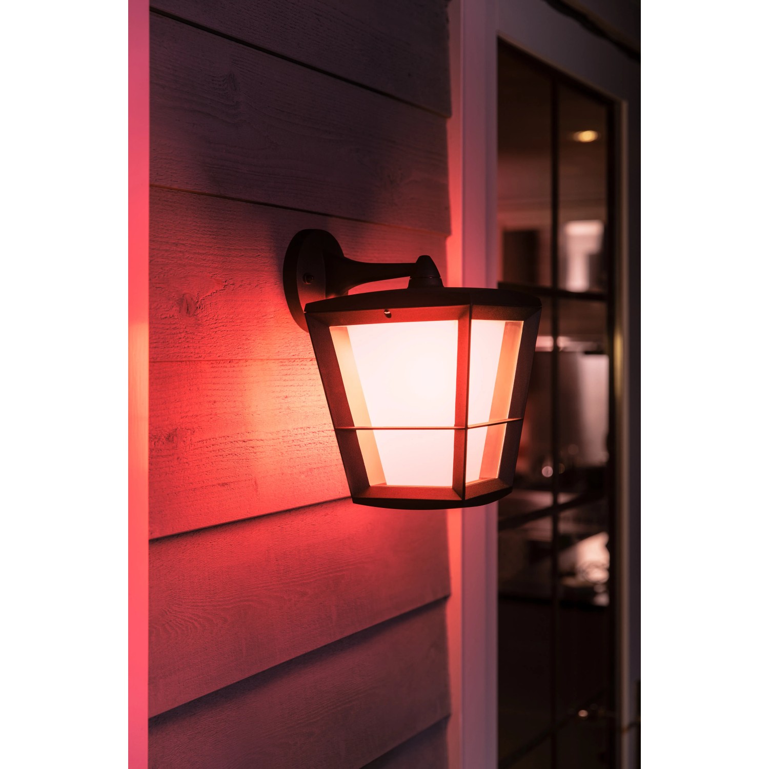 Hängende Philips Hue Econic LED-Laterne in Schwarz mit farbigem Licht an Hauswand.