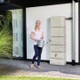4rain Zisterne Slim Stone Decor Regentonne in Sandbeige (330 l) mit Frau und Gießkanne.