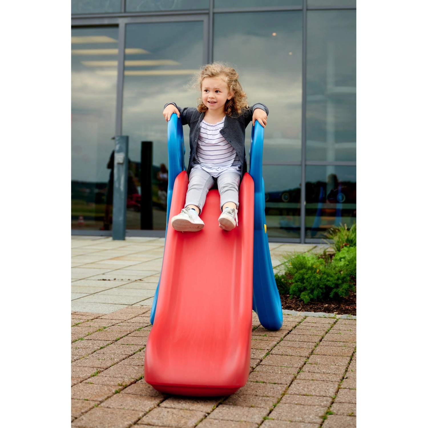 Kind rutscht auf der roten BIG Fun Slide Rutsche mit blauem Rahmen im Garten.