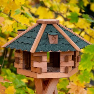 Sechseckiges Dobar Blockhaus Vogelhaus aus Kiefernholz mit grünem Bitumendach, im Garten stehend.