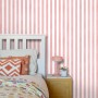 ESTAhome Vliestapete mit rosa-weißem Streifenmuster an einer Wand, daneben ein weißes Bett. Dekorative Tapete.