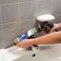 Person dichtet Waschbecken mit weißem Soudal Sanitär Express Silikon aus Kartuschenpistole ab. Fliesenwand im Bad.