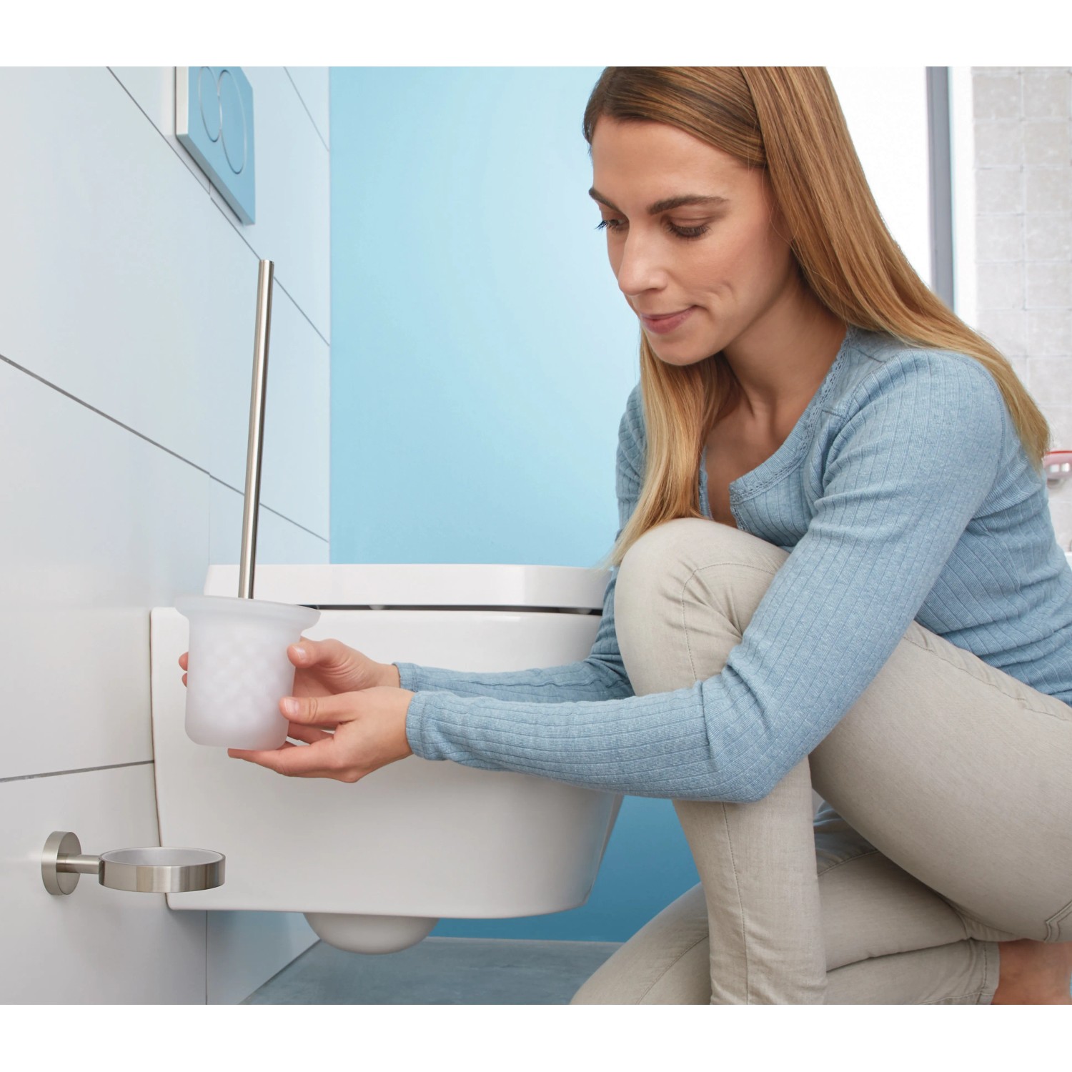 Frau setzt Tesa WC-Bürstengarnitur Moon Edelstahloptik in Halterung ein.