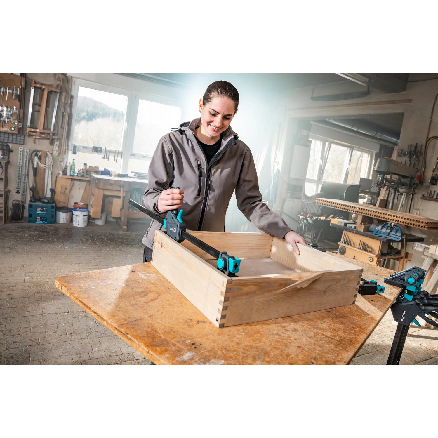 Frau fixiert Holzkiste mit Wolfcraft Einhandzwinge Pro Max 150 mm. Spannwerkzeug im Einsatz.