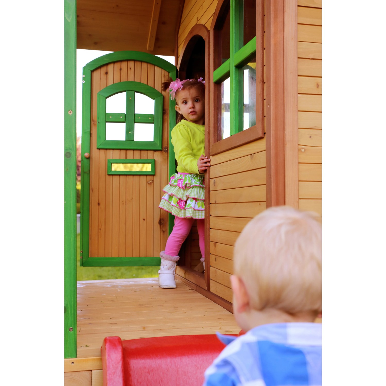 Axi Tom Spielhaus aus Holz mit roter Rutsche, braun-grün, mit spielenden Kindern.