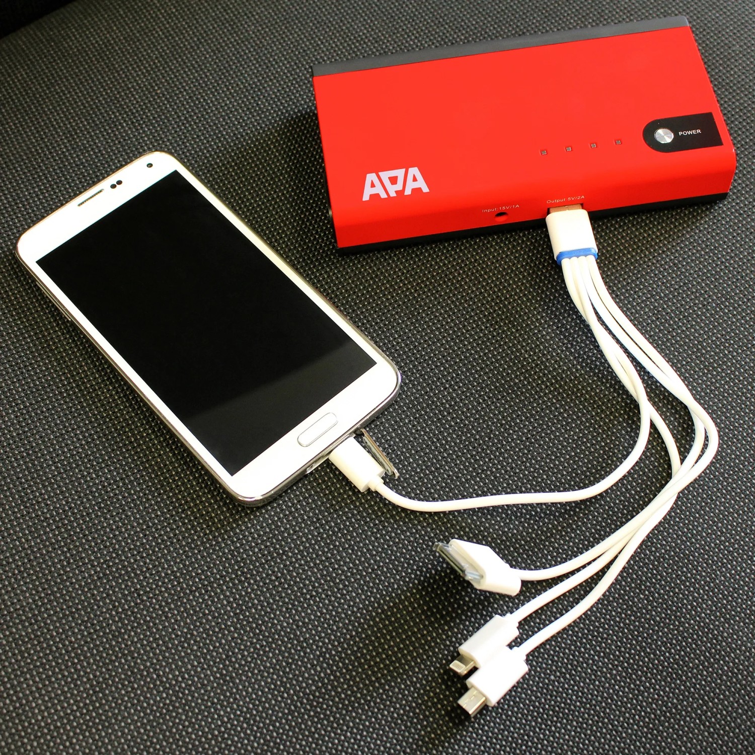 Mini Lithium Power Pack lädt Smartphone. Rote Powerbank mit LED-Leuchte und Ladekabel.