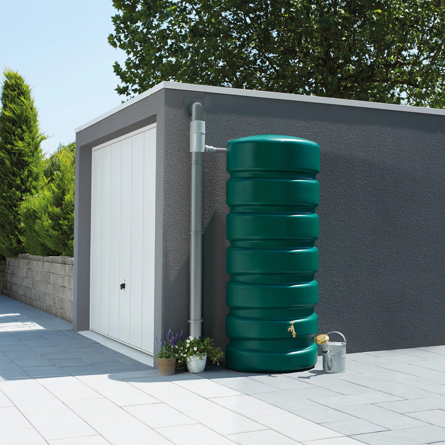 Garantia Zisterne Classico 650 l, dunkelgrün, neben einem Fallrohr an einer Garage. Regentonnen für Garten.