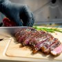 Angeschnittenes Steak vom Taino Platinum Gasgrill auf Holzbrett mit Messer und Hand.