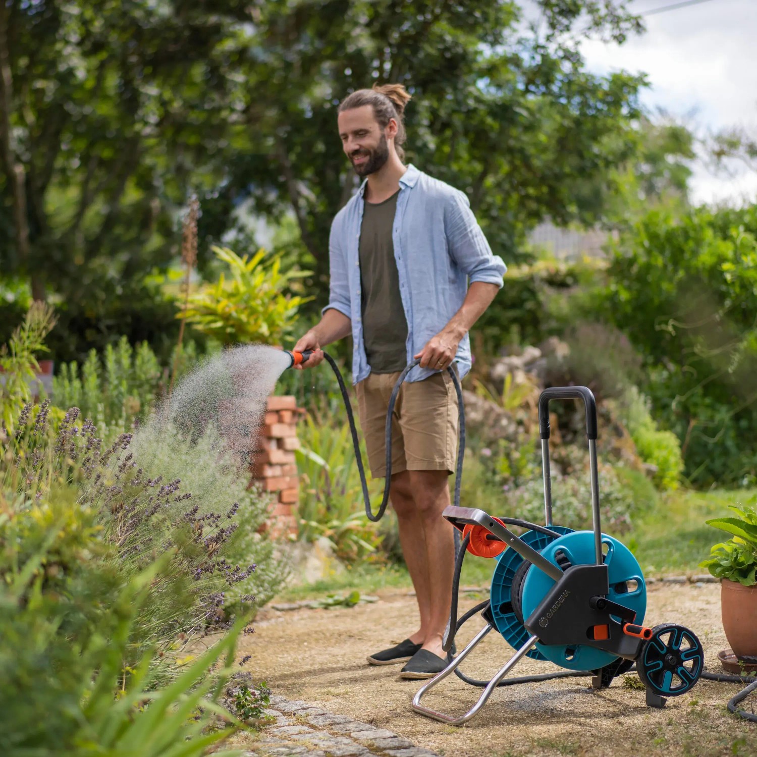 Mann bewässert Garten mit Gardena Gartenschlauch-Set Liano™ Life 10m und Schlauchwagen.