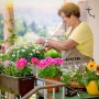 Braune Gusseisen Vogeltränke mit Vogel-Figur an Wand. Frau gärtnert auf Balkon mit Blumen. Für Garten & Terrasse.