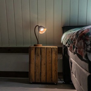 Rustikale Tischleuchte Rax in Rostbraun mit Holzfuß auf einem Nachttisch im Schlafzimmer.