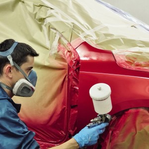 Mann lackiert Auto rot mit Farbspritzpistole und Kompressor. Schutzmaske und Abdeckung vorhanden.