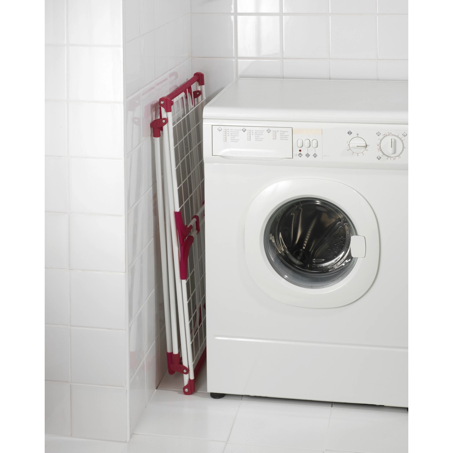 Zusammengeklappter, weiß-pinker Wenko Wäscheständer Summer Dry neben einer Waschmaschine.