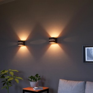Zwei schwarz-goldene SSC-LUXon KOURA Wandleuchten mit Up-Down-Licht und Lichtschlitz an grauer Wand.