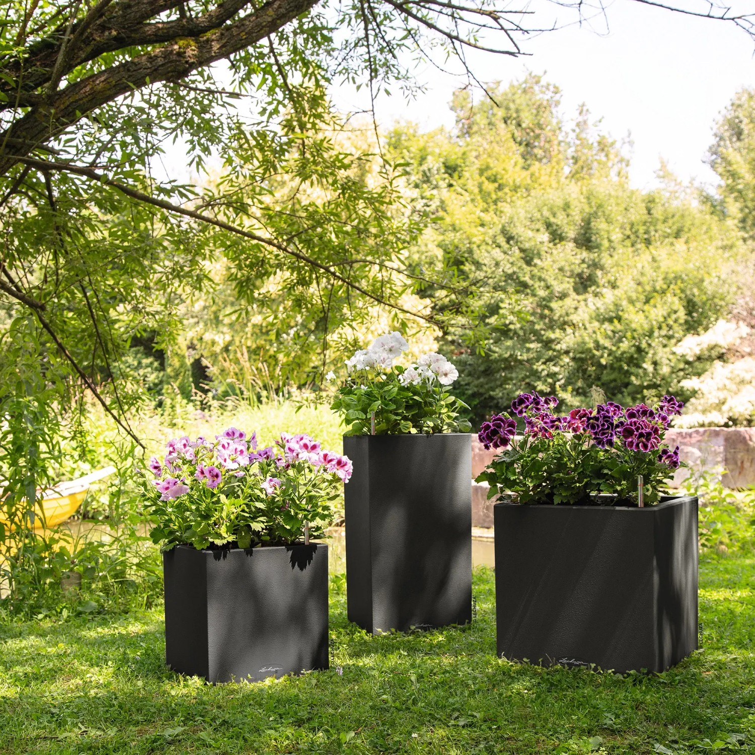 Lechuza Canto Stone Pflanzsäulen in Graphitschwarz mit bunten Blumen auf einer Wiese.