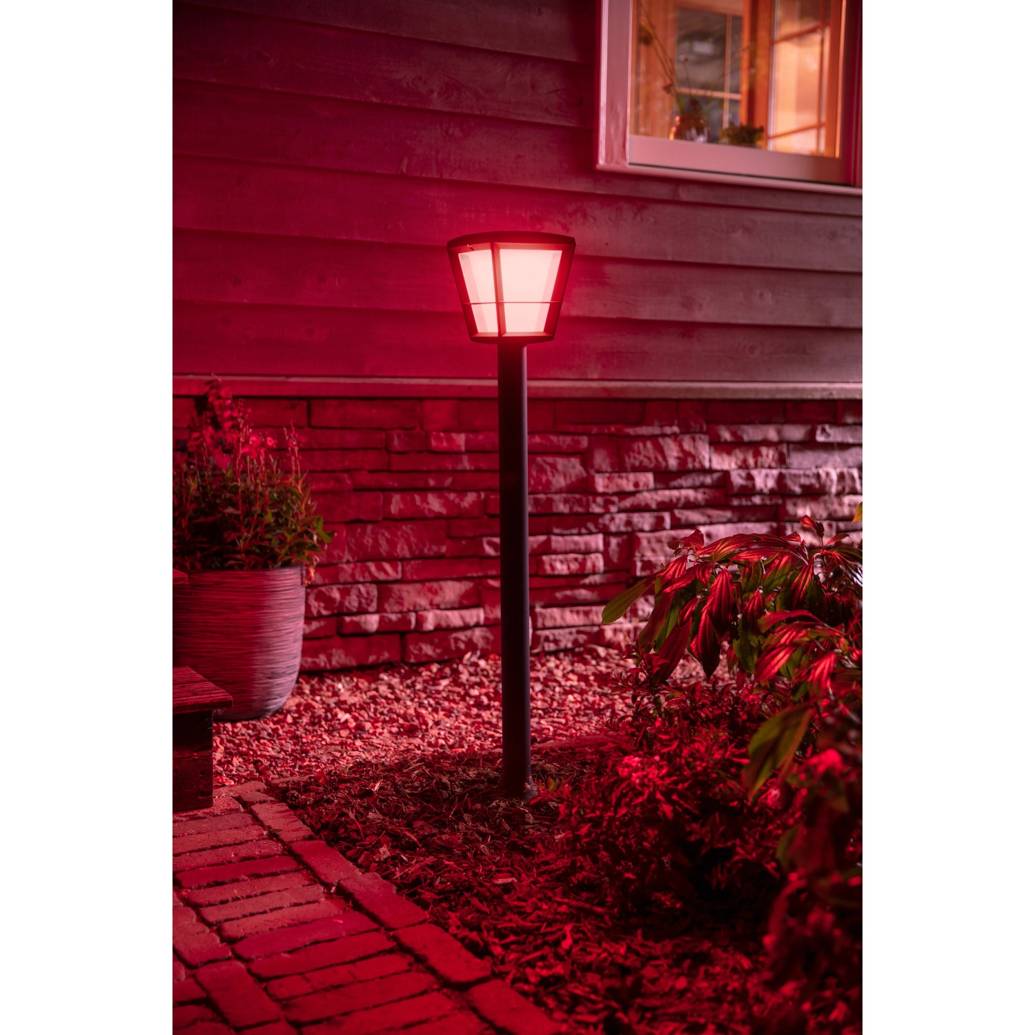Philips Hue Econic LED-Wegeleuchte in Schwarz, leuchtet rot im Garten.