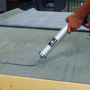 Hand trägt EPDM Anschluss- & Flächenkleber mit Kartuschenpistole auf graue Dachfolie auf.