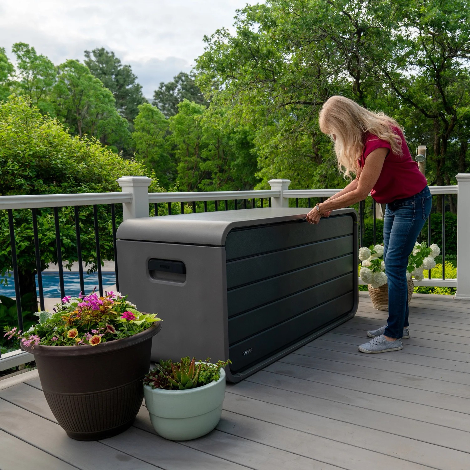Graue Lifetime Kissenbox (625 l) auf Terrasse mit Frau beim Öffnen. Praktische Aufbewahrungsbox für Garten.