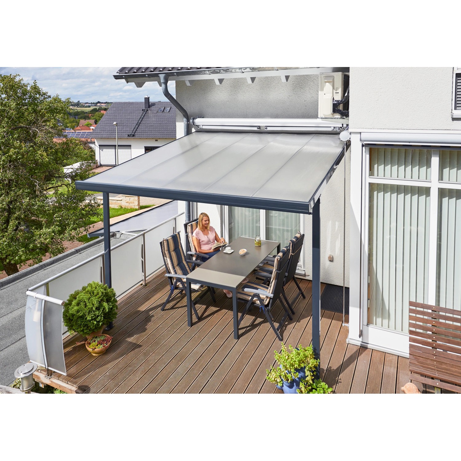 Moderne Gutta Terrassenüberdachung in Anthrazit mit Polycarbonatplatten und sitzender Person am Tisch.