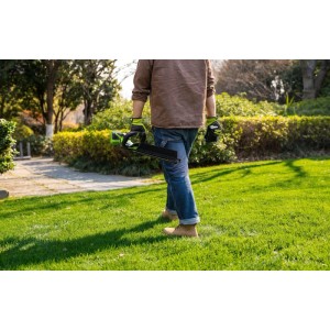 Person trägt Greenworks Akku-Heckenschere im Garten. Grüne Akku-Heckenschere für Heckenpflege.