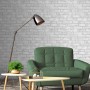Graue Erismann Vliestapete in Steinoptik an Wand hinter Sessel und Lampe.