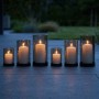 6er Set Windlichter aus Rauchglas mit schwarzen Eisenfüßen in 3 Größen, brennende Kerzen auf dunklem Boden.